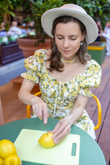 A woman in a floral dress slices a lemon, creating a fresh and vibrant atmosphere in a cozy outdoor setting