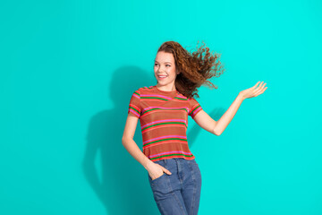 Smiling young woman with wavy hair making a welcoming gesture while wearing a striped shirt against...