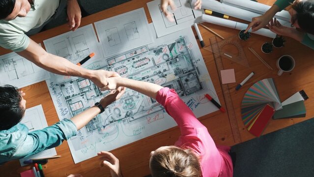 Top view of skilled civil engineer team shaking hand while discussing idea at meeting table with color palettes and equipment. Top aerial view of diverse people clap hands and shake hands. Symposium.