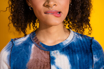 Close-up of a Young Woman with Stylish Curly Hair Biting Her Lip Against a Bright Yellow Background