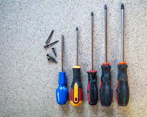 Screwdrivers of varying sizes with screws on a grey surface