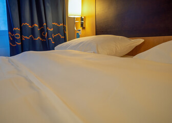 large double bed with white linen and large pillow included wall lamp warm light.