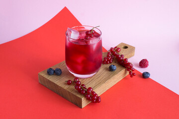 Cold lemonade or cocktail with red currants in the drinking glass on a red and pink background....
