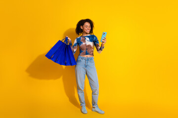 Young Stylish Woman Holding Shopping Bags and Smartphone Against a Yellow Background