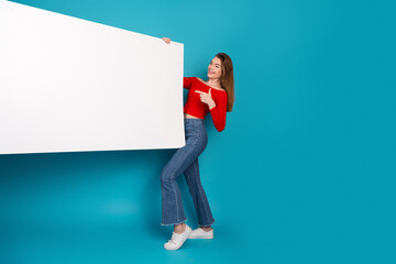 Young woman pointing to a blank white banner on a vibrant blue background, conveying a cheerful and...