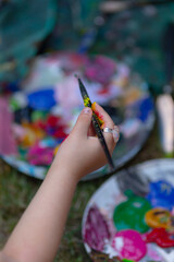 A person is holding a paintbrush in front of a colorful palette filled with various types of paint,...