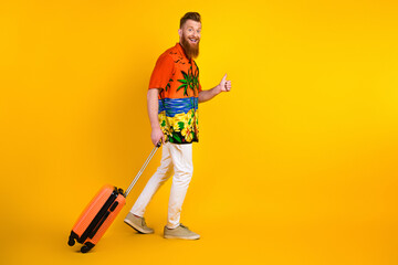 Stylish young man with tropical printed outfit carrying luggage giving a thumbs up gesture over...
