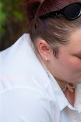A woman dressed in stylish sunglasses and a crisp white shirt is looking down at something with a...