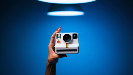 Naklejka premium Hand Holding a White Instant Camera with Rainbow Stripe Under a Spotlight