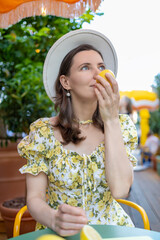 A woman in a floral dress sits outdoors, holding a lemon to her face, creating a fresh and playful atmosphere