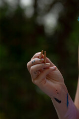 A woman s hand, which has some paint on it, is firmly holding a piece of wood with her fingers wrapped around it gently in a firm grip