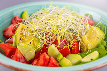Fresh avocado and tomato salad with sprouts in a turquoise bowl