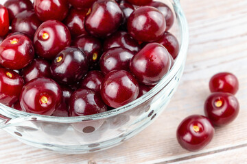Fresh juicy red cherries in glass bowl on wooden table