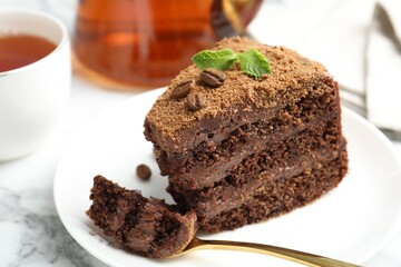 Piece of delicious chocolate cake with coffee beans, mint and fork on white marble table, closeup