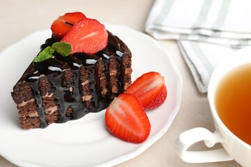 Piece of chocolate cake served with strawberries and tea on white table, closeup