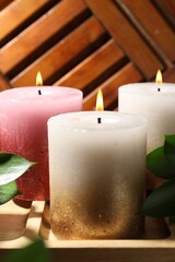 Burning candles and green leaves on wooden tray, closeup