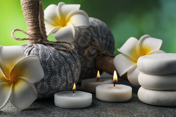 Herbal bags, spa stones, plumeria flowers and burning candles on grey table, closeup
