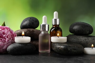 Spa composition with wet stones, cosmetic products and burning candles on dark textured table...