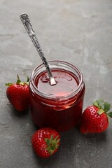 Tasty homemade strawberry jam and berries on grey table, closeup