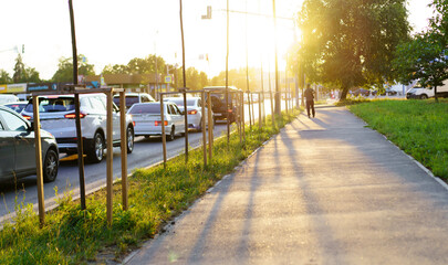 Late afternoon sunlight illuminates a busy street and sidewalk with passing cars and a lone pedestrian