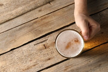 Man with glass mug of beer at wooden table, top view. Space for text