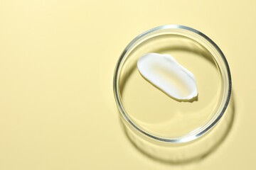 Cosmetic product in Petri dish on pale yellow background, top view. Space for text