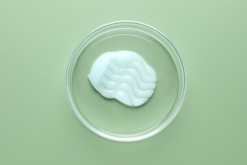 Cosmetic product in Petri dish on green background, top view