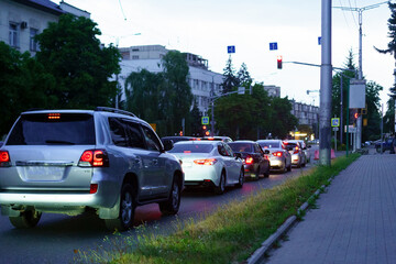 Traffic congestion at dusk on a city street with varied vehicles waiting at a red light