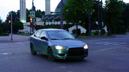 Car driving on the street near urban architecture during twilight hours in a city setting