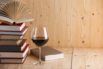 Glass of red wine and stacked books on wooden table. Space for text