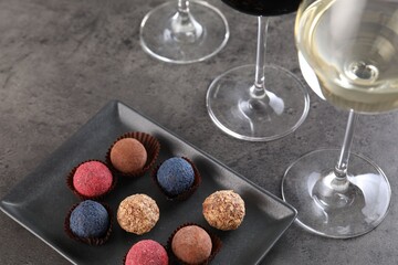 Tasty truffle bonbons and wine on grey table, above view