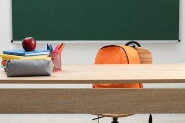 Different school stationery and red apple on wooden table near blackboard indoors