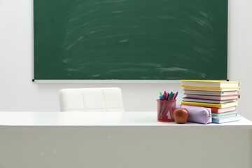 Different school stationery and apple on white table near blackboard indoors