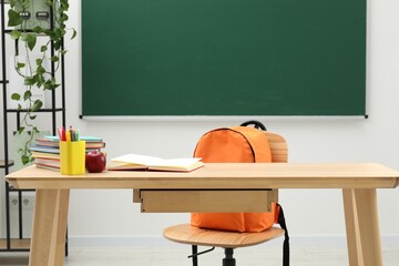 Different school stationery and red apple on wooden table near blackboard indoors