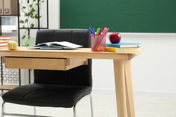 Different school stationery and red apple on wooden table near blackboard