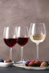 Delicious truffle bonbons and wine on black table against grey background