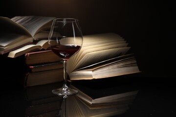 Red wine in glass and stack of books on mirror table against dark background, closeup