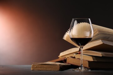 Glass of tasty wine and books on dark textured table in color lights, closeup. Space for text