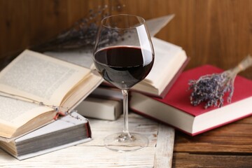 Red wine in glass and books on wooden table, closeup
