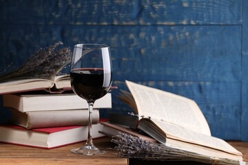 Red wine in glass, lavender flowers and books on wooden table against blue background, closeup