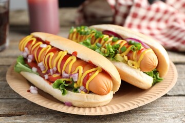 Delicious hot dogs with sauces, lettuce and onion on wooden table, closeup