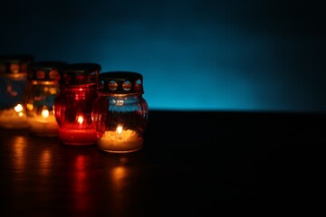 Many grave candles on black table against blue background, closeup. Space for text