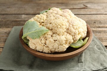 Fresh cauliflower with green leaves on wooden table, closeup