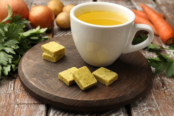 Aromatic bouillon cubes, broth, parsley and vegetables on wooden table, closeup