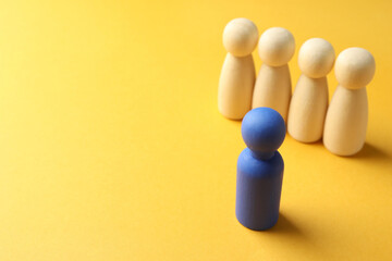 Unemployment. One blue figure among wooden on yellow background, closeup. Space for text