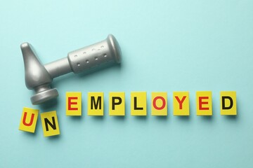 Word Unemployed and hammer on light blue background, flat lay