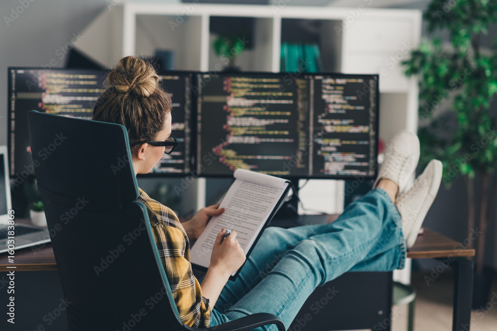 Poster young female programmer working remotely from home office with dual monitors reviewing code and tech