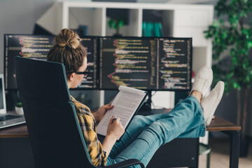 Young female programmer working remotely from home office with dual monitors reviewing code and...