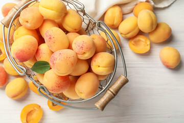 Fresh ripe apricots in metal basket on white wooden table, flat lay