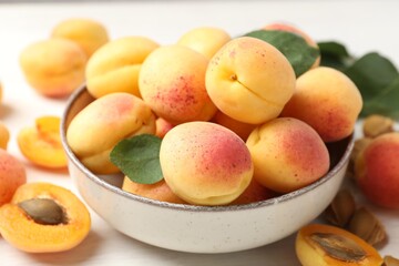 Fresh ripe apricots in bowl and green leaves on white table, closeup